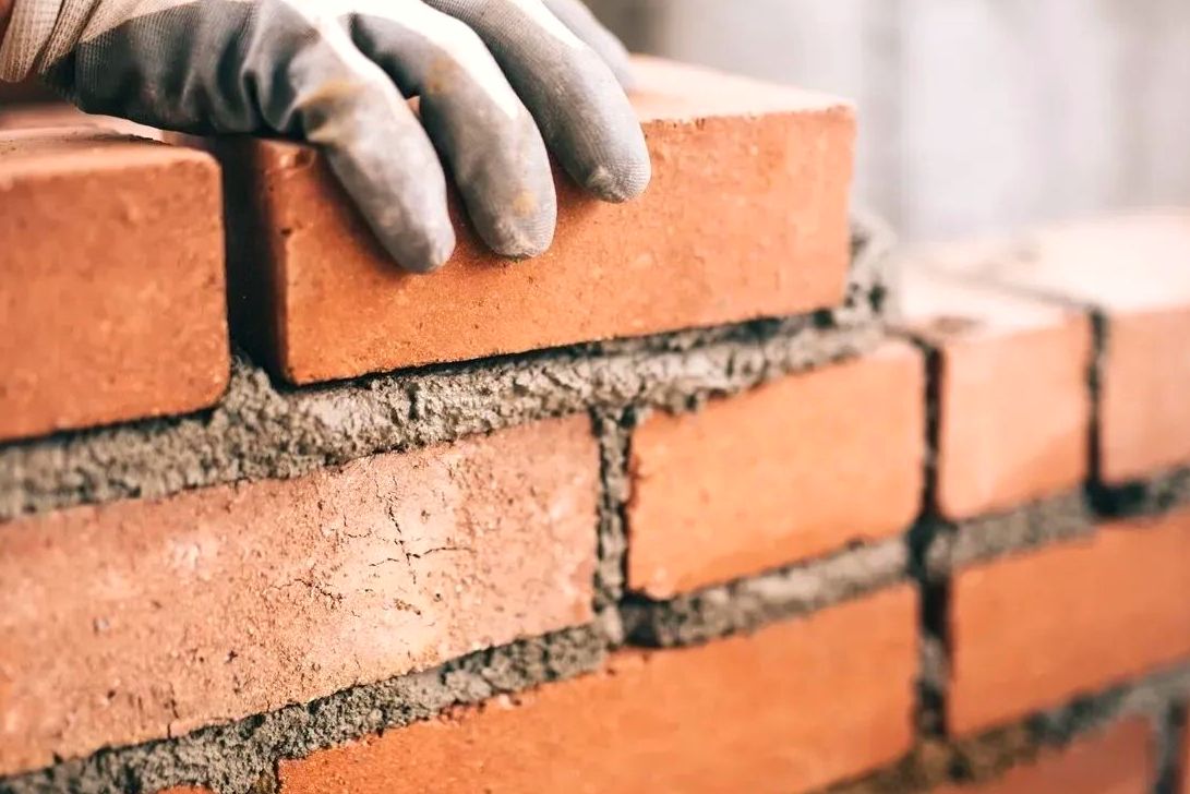 Gloved hand setting a brick into a fresh mortar bed